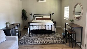 A bedroom with a bed, bedside tables, a desk, a chair, a potted plant, a mirror, and a chandelier. - Charming cottage with WiFi and AC on a Ranch setting in Oakdale (Oakdale)