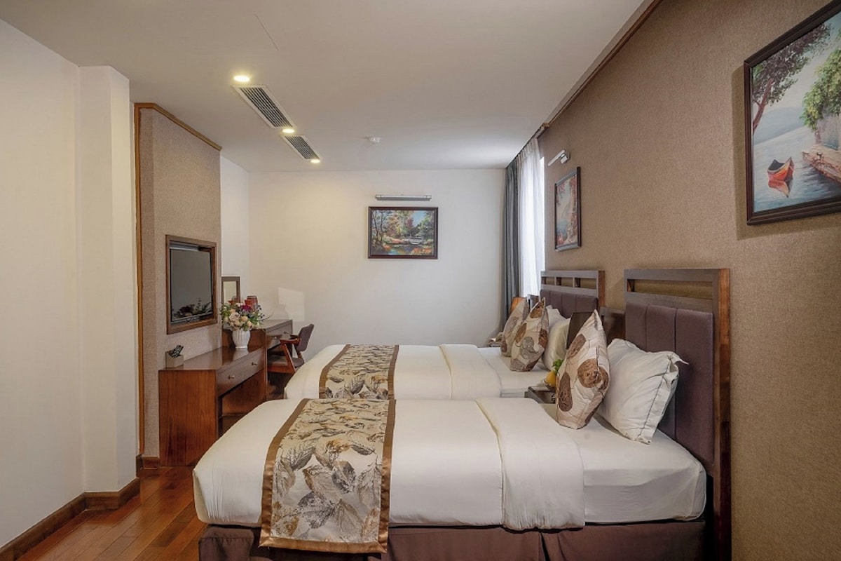 Une chambre d’hôtel avec deux lits, un bureau, une chaise, un miroir et des œuvres d’art accrochées aux murs.
