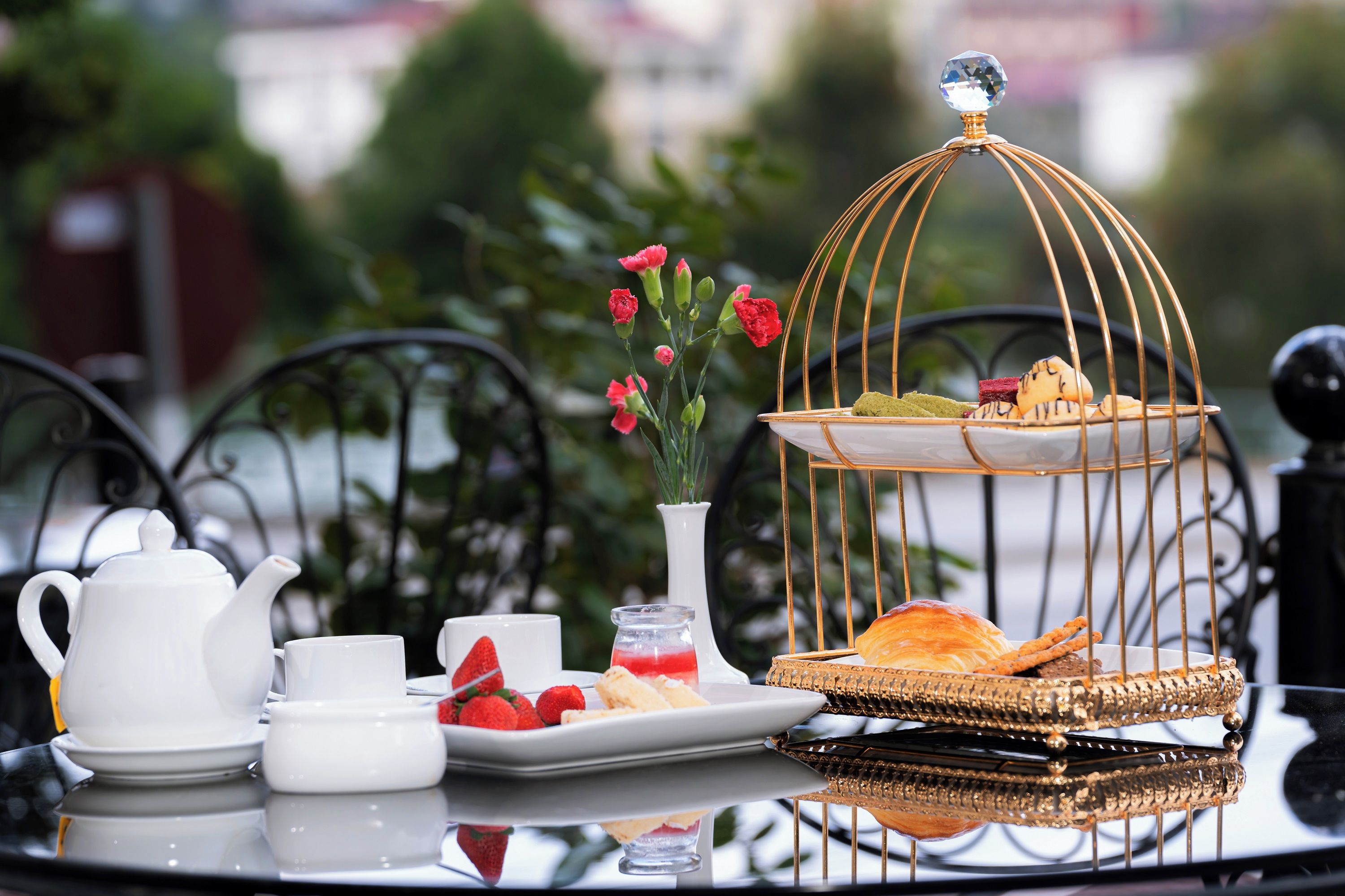 A table set with a teapot, cups, a plate with strawberries, a small vase with flowers, and a decorative birdcage with pastries.