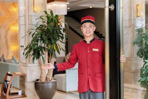 Een hotellobby met een grote potplant, een receptiebalie en een trap op de achtergrond.