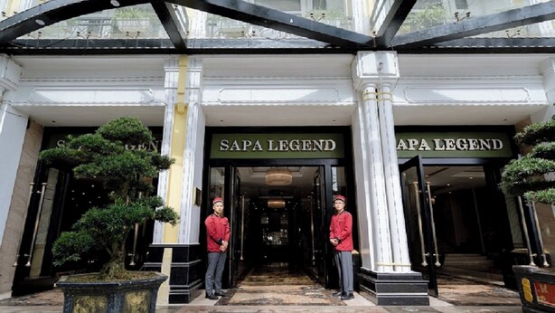 Entrada de l'hotel Sapa Legend, amb dos empleats uniformats a la porta, una gran arcada i un jardí ben cuidat amb un bonsai.