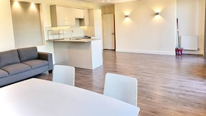 A modern living room with a sofa, a dining table, and a kitchen area.