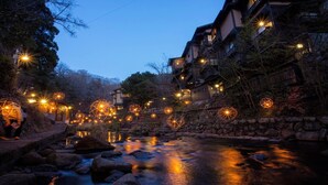 A traditional Japanese ryokan with a stone pathway leading to a river, surrounded by trees and illuminated by hanging paper lanterns. - Container House Villa Kurokawa　 (Minamioguni)