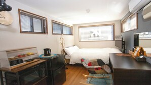 A compact hotel room with a bed, a desk, a chair, and a small kitchenette. - Container House Villa Kurokawa　 (Minamioguni)
