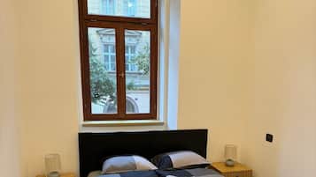 A bedroom with a large bed, two bedside tables, a window, and a view of buildings outside.