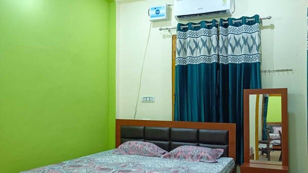 A bedroom with a bed, a ceiling fan, an air conditioning unit, a mirror, and a window with curtains. - Om home stay (Faizabad)