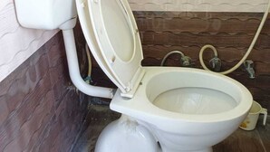 A toilet with a white seat and lid, a white tank, and a brown tiled floor. - Om home stay (Faizabad)