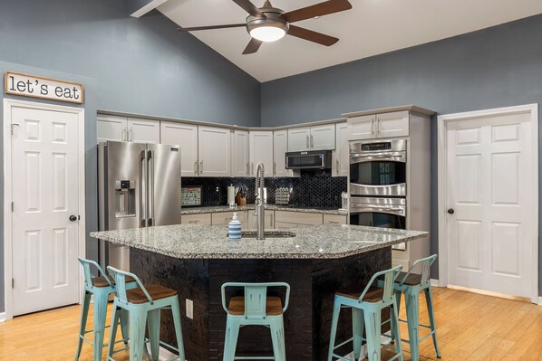 A modern kitchen with a central island, white cabinets, stainless steel appliances, and teal bar stools. - Cozy 4bd lakefront home in Lake Lanier w/ HotTub, FirePit, Private dock, Wifi (Gainesville)