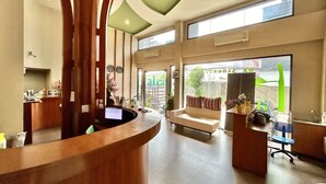 Un espace d’accueil avec un bureau incurvé, un canapé et un fauteuil. De grandes fenêtres offrent une vue sur l’extérieur.