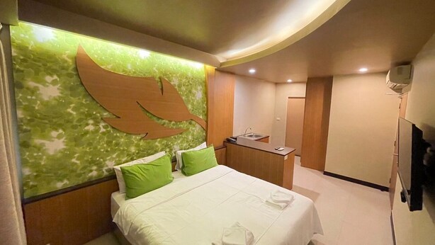 Une chambre d’hôtel avec un lit, des oreillers verts, un petit bureau avec un lavabo et un téléviseur fixé au mur.