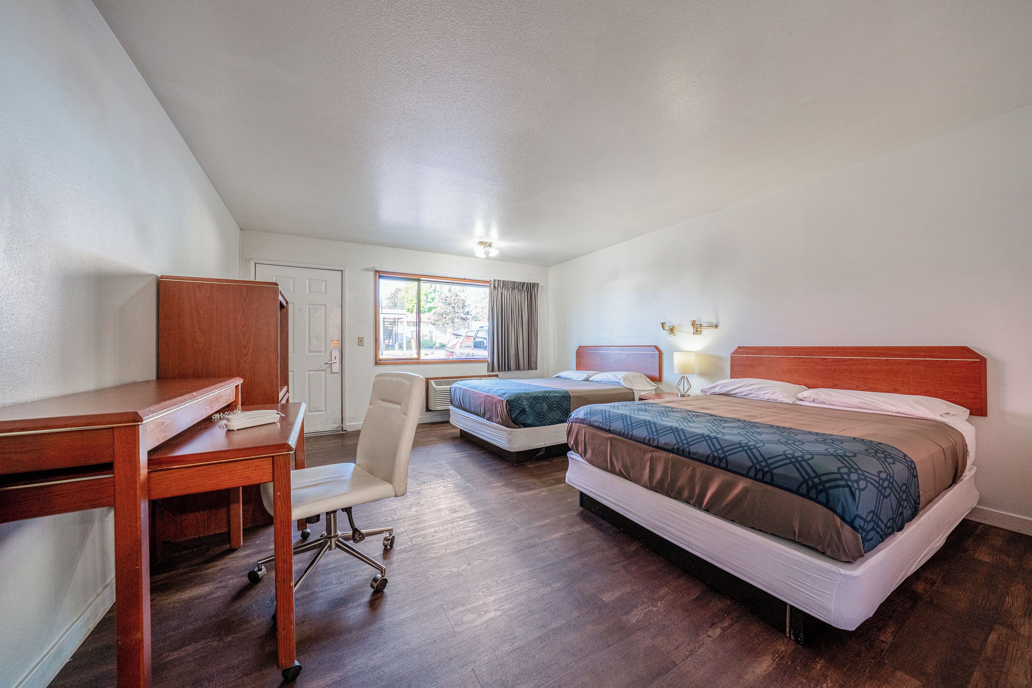 Habitación de hotel con dos camas, un escritorio, una silla y una ventana con cortinas.