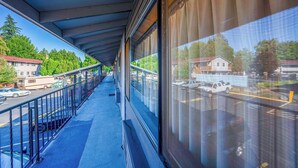 A covered outdoor corridor with a blue floor, metal railing, and large windows offering views of a parking lot and buildings.