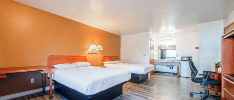 A hotel room with two beds, a desk, a chair, and a kitchenette.
