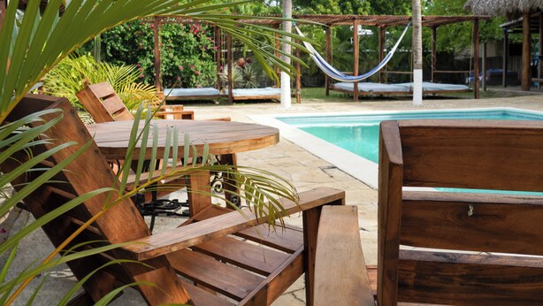 A wooden deck with lounge chairs and a hammock by a pool, surrounded by tropical plants and a thatched-roof structure. - Hotel Ingigante Poolside Room (El Gigante)
