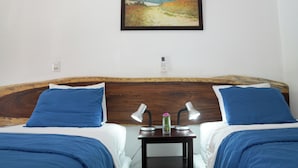 A hotel room with two beds, a wooden headboard, a nightstand with lamps, and a painting on the wall. - Poolside Family Room with 2 twin beds (El Gigante)