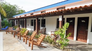 A building with a tiled roof, multiple doors, and a covered outdoor seating area with wooden chairs and tables. - Poolside Family Room with 2 twin beds (El Gigante)