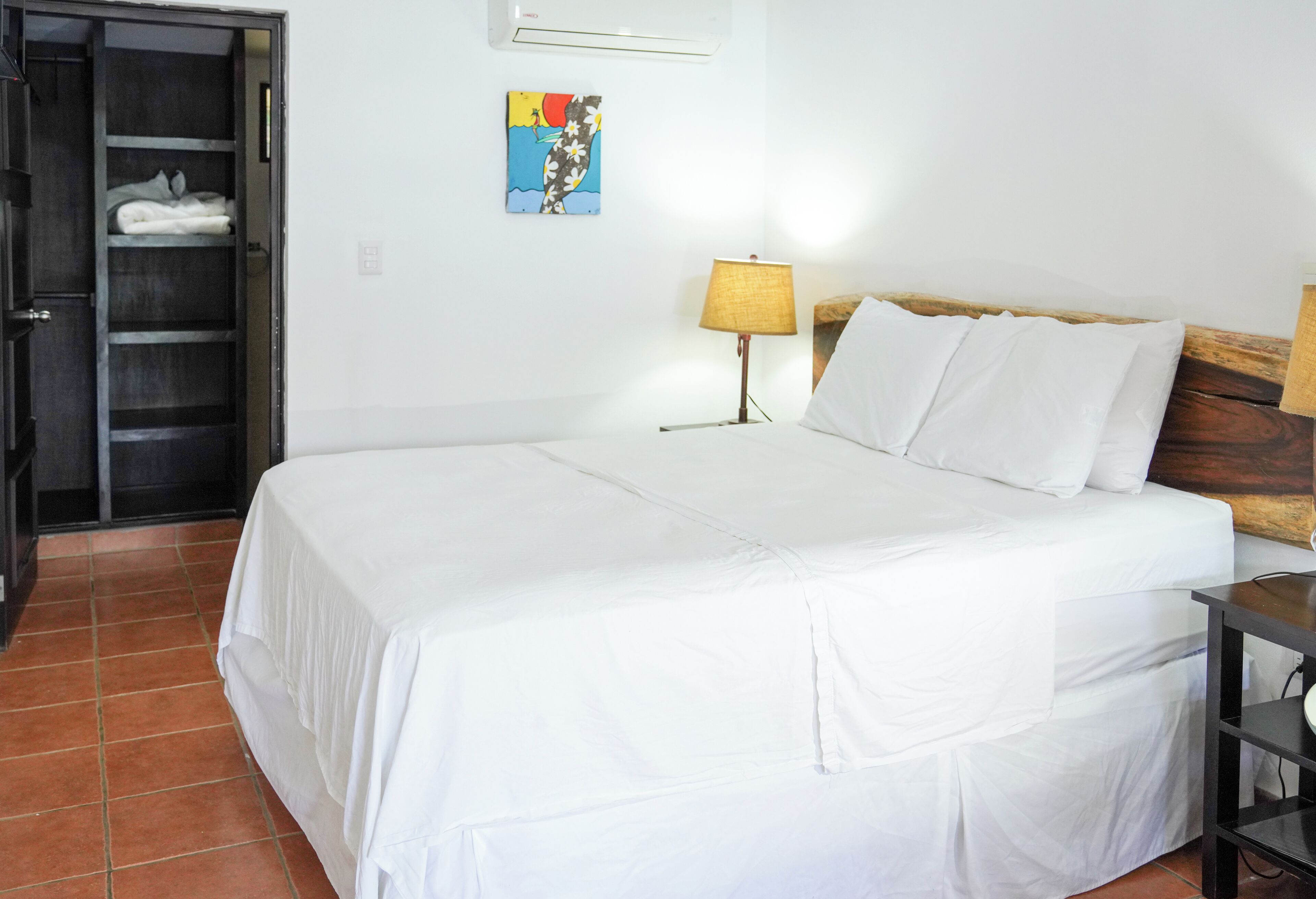 A hotel room with a large bed, a wardrobe, a painting on the wall, and a lamp.