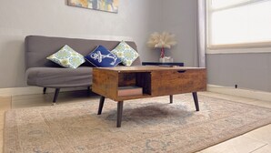 Un salon avec un canapé gris, des coussins à motifs, une table basse en bois, un tapis et un tableau accroché au mur.