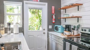 A kitchen with a white door, a microwave, a stove, and shelves with dishes and jars.