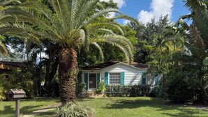A house with a front porch, surrounded by lush greenery and palm trees.