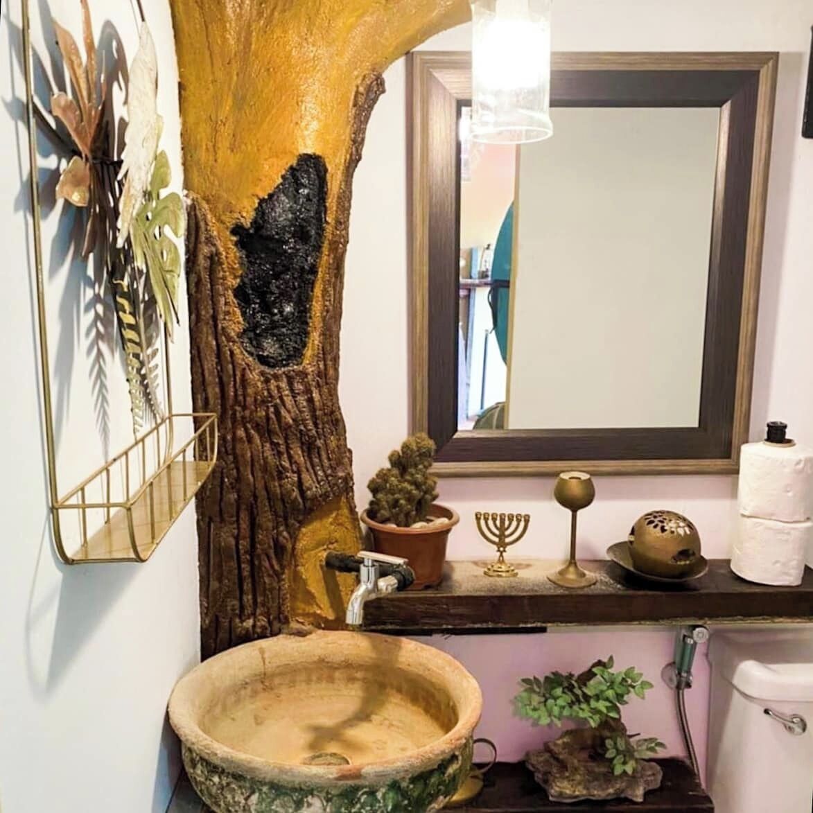 A bathroom with a large tree trunk, a wooden sink, a mirror, and various toiletries on the counter.