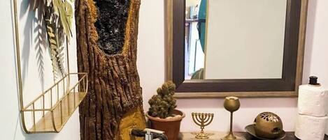 A bathroom with a large tree trunk, a wooden sink, a mirror, and various toiletries on the counter.