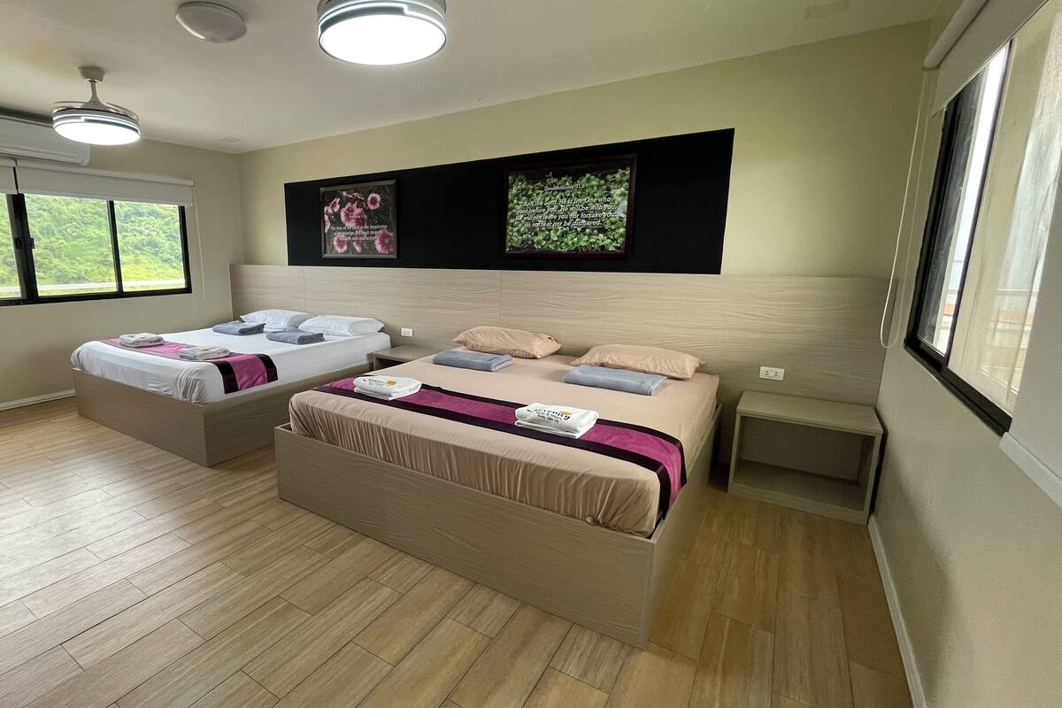 Une chambre d’hôtel moderne avec deux lits, une grande fenêtre et un ventilateur de plafond.