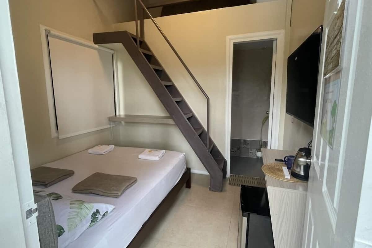 Une pièce de taille modeste comprenant un lit, une petite kitchenette, un téléviseur et un escalier.