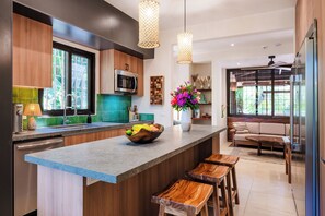 A modern kitchen with a central island, wooden bar stools, a built-in microwave, and a large window.
