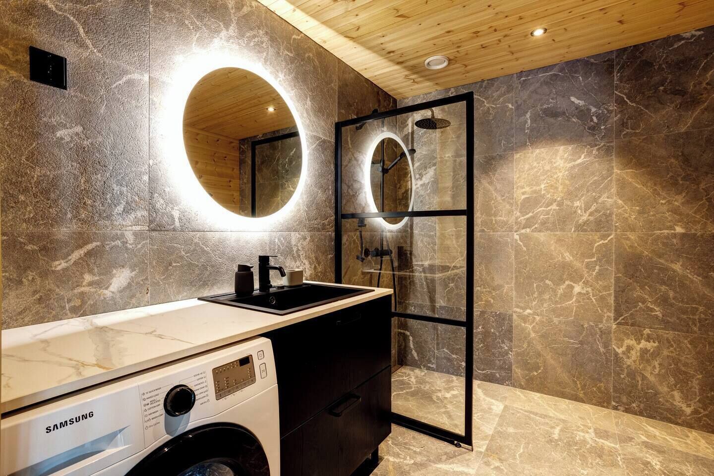 Une salle de bain moderne équipée d’un lave-linge intégré, d’un lavabo et d’un espace douche.