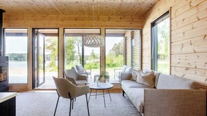 Ein modernes Interieur mit Holzbalkendecke, großen Fenstern, einer Couch, Sesseln und einem Tisch.