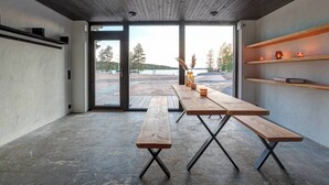 Ein modernes Interieur mit einem großen Holztisch und Bänken, Blick auf den Strand und Regalen mit Kerzen.