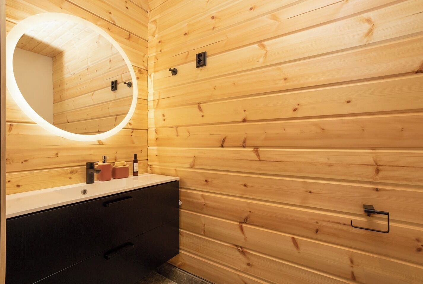 A wooden cabin bathroom with a round mirror, a sink, and a dark cabinet.