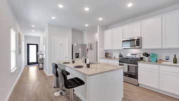 A modern kitchen with white cabinetry, a granite countertop, stainless steel appliances, and a bar area with stools.