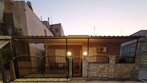 A gated residential area with a stone wall and metal gate, a paved driveway, and a building with a flat roof and satellite dish. - RENT HOUSE ROOMS KALAMATA  (Agios Dionisios)