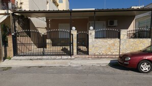 A residential house with a stone facade, a black metal gate, and a red car parked in front. - RENT HOUSE ROOMS KALAMATA  (Agios Dionisios)
