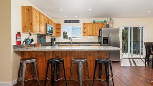 A modern kitchen with wooden cabinets, a stainless steel refrigerator, and a large island with bar stools. - Makena's -near beach, game room, hot tub, dog ok (Pacific City)