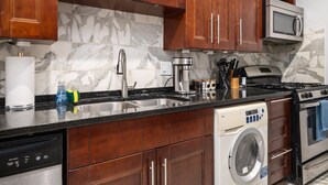 Una cocina con armarios de madera, un lavamanos de acero inoxidable, una cafetera, un microondas, una estufa y un lavavajillas.