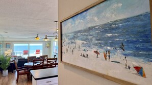 A dining area with a large painting of a beach scene. - Beachfront Oasis with Dual Balconies, Pool, Hot Tub & Stunning Sunset Views in Madeira Beach (Madeira Beach)