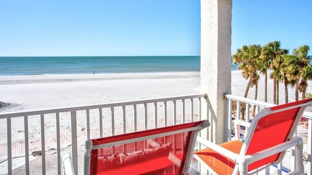 A beach view from a balcony with white railings and red and white chairs. - Beachfront Oasis with Dual Balconies, Pool, Hot Tub & Stunning Sunset Views in Madeira Beach (Madeira Beach)