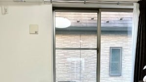 A room with a bed, a dark green sofa, a window with a view of a brick building, and a wooden floor. - Gracious Higashi Shinjuku (Tokyo)