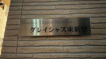 A sign on a stone wall with the text "Gracious Higashi Shinjuku" and "グレイシジャス東新宿" in English and Japanese.