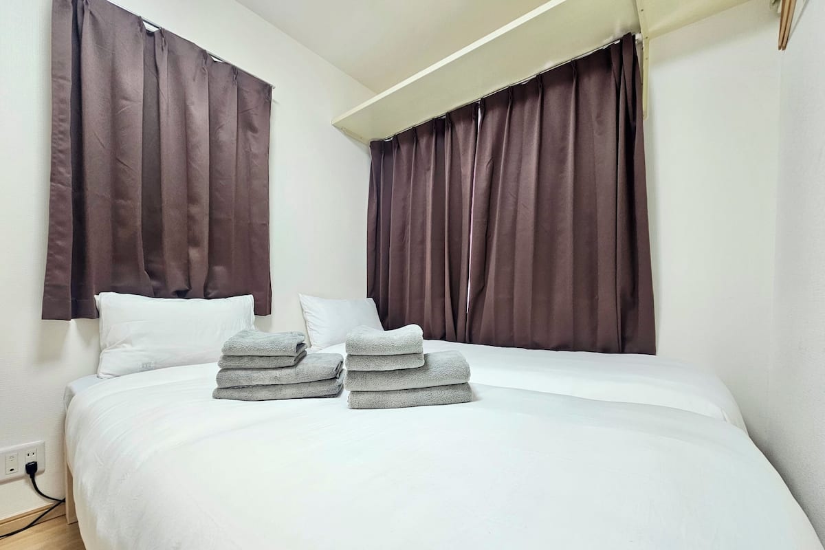 A hotel room with a bed, white bedding, brown curtains, and a stack of towels.