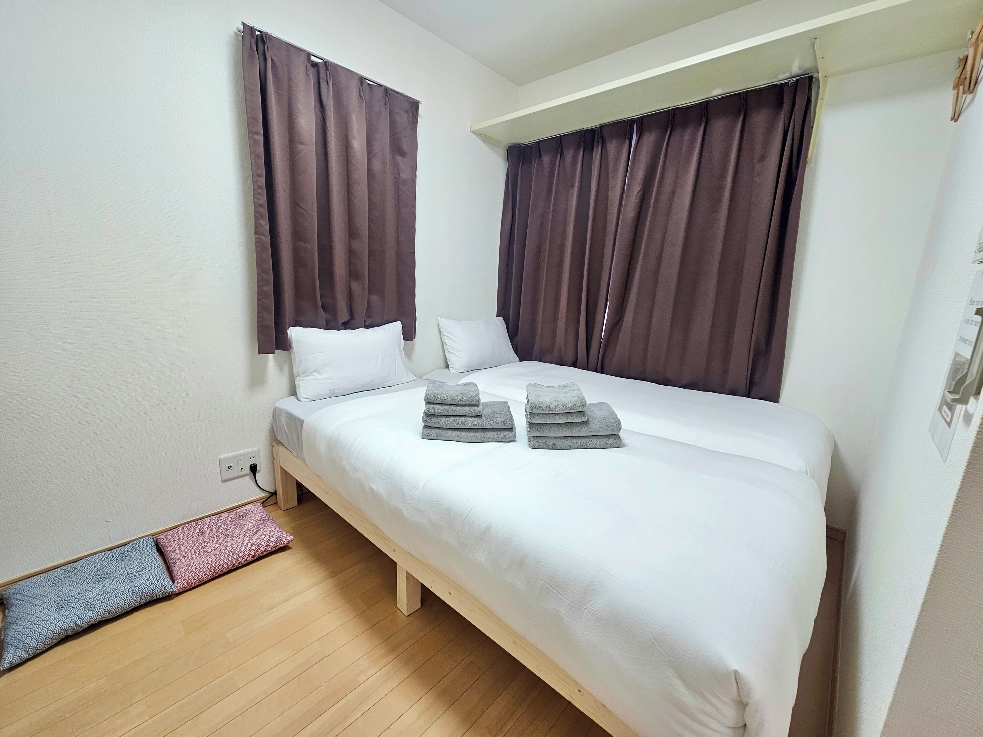 Una cama individual con colchón y almohadas blancos, suelo de madera y cortinas marrones.