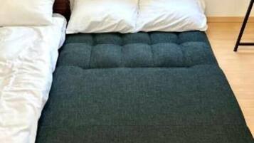 A bed with a dark mattress and white pillows, a window with a view of a brick wall, and a wooden floor.