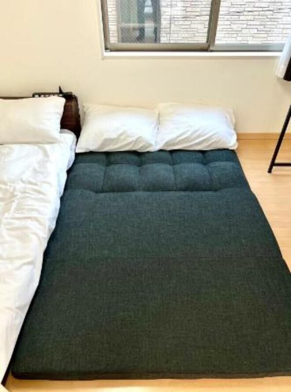 A bed with a dark mattress and white pillows, a window with a view of a brick wall, and a wooden floor.