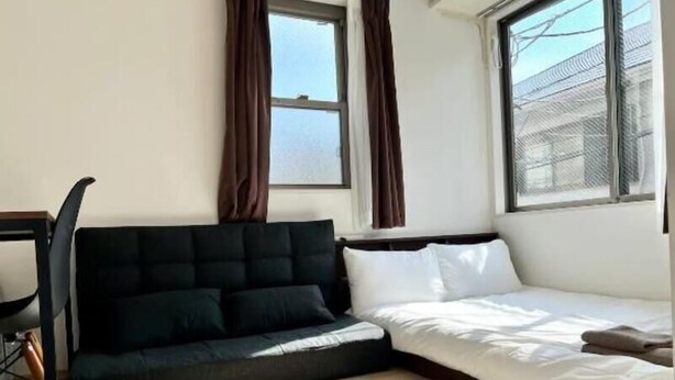 A room with a bed, a dark sofa, a chair, and a window with curtains. - Gracious Higashi Shinjuku (Tokyo)