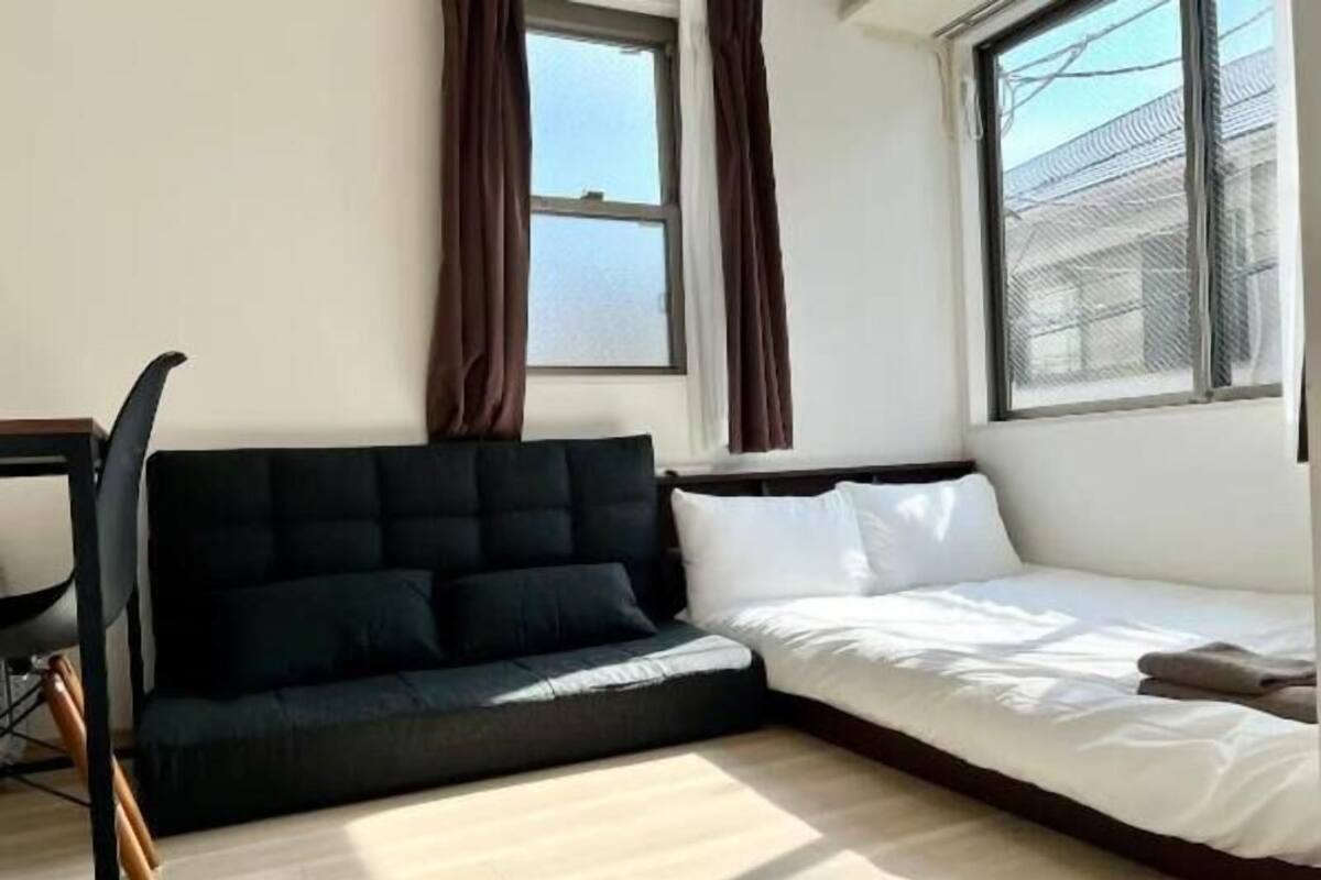 A room with a bed, a dark sofa, a chair, and a window with curtains.