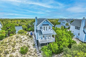 A coastal house with a balcony, surrounded by greenery and other houses.