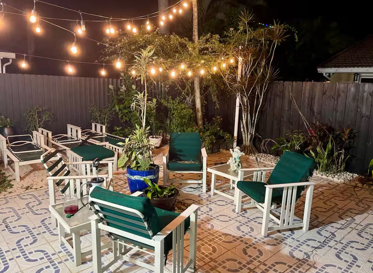 An outdoor patio with white and green chairs, string lights, and potted plants.
